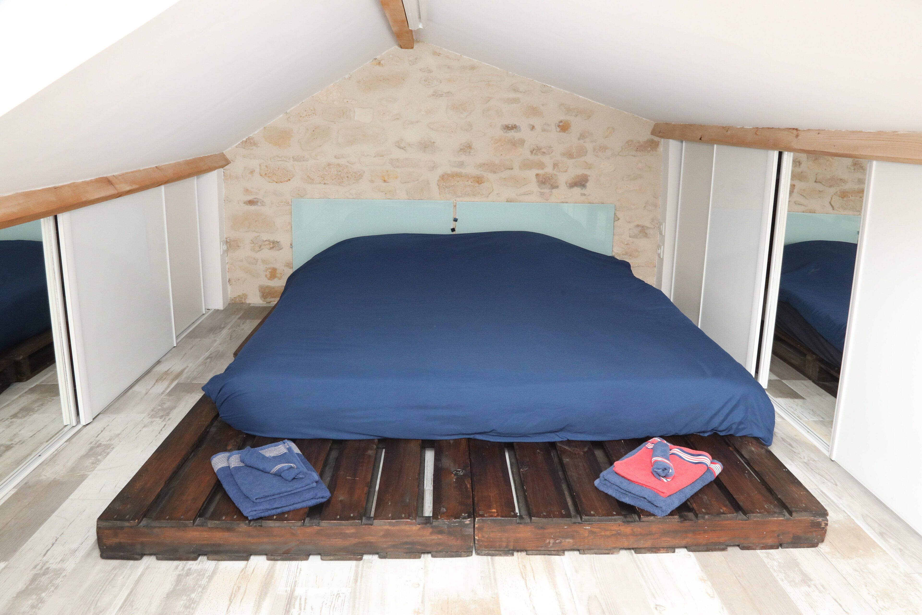 A room with a sloped ceiling, a bed with a blue mattress, and a wooden platform.