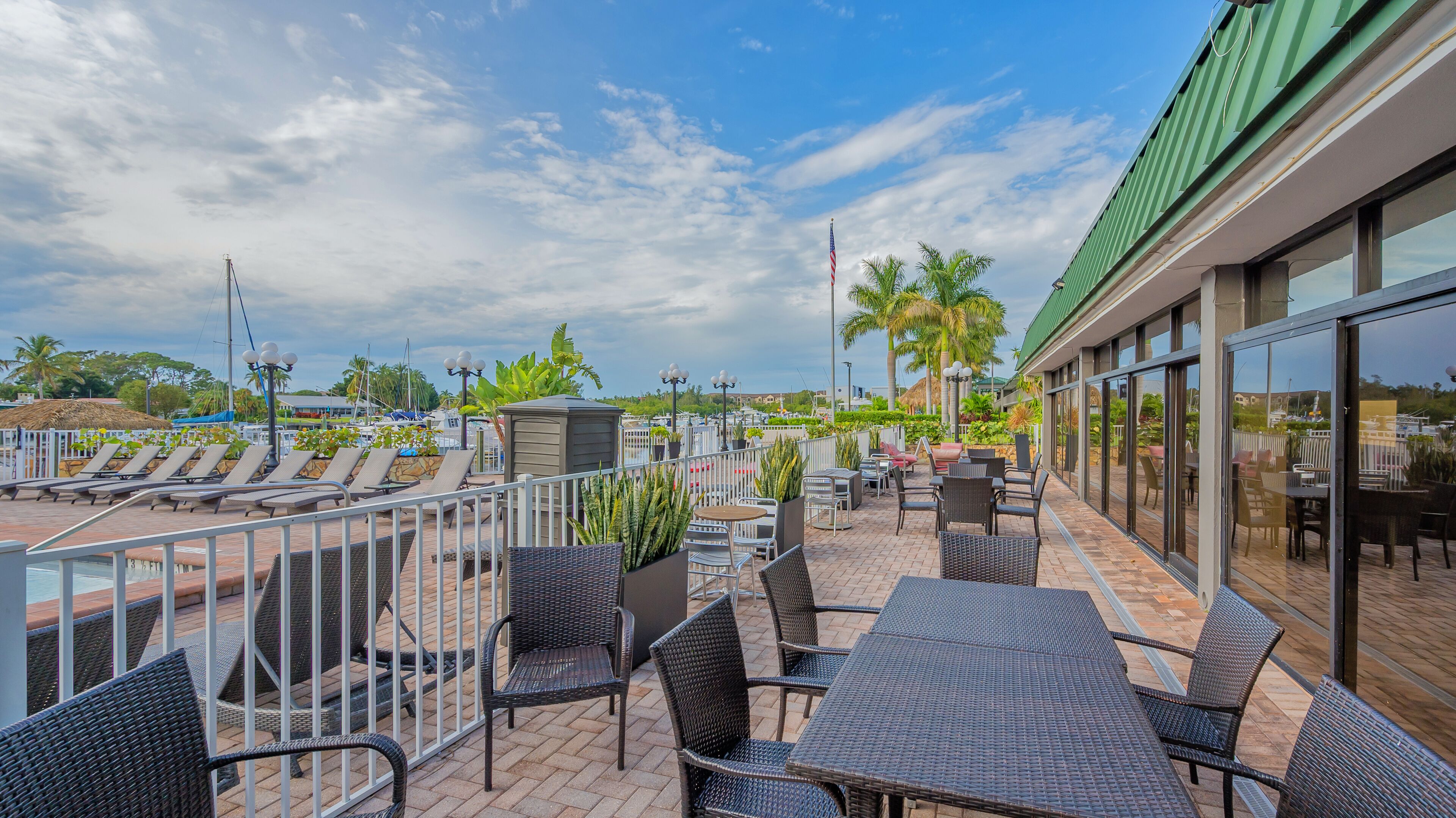 Terraza en la azotea con sillones, mesas y sillas, con vista a un puerto deportivo con barcos y palmeras.