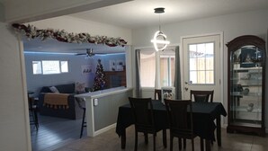 A dining area with a table and chairs, a Christmas tree, and a kitchen in the background.