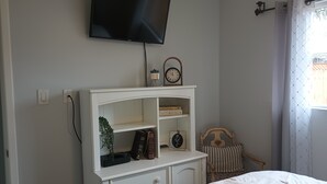 A bedroom with a bed, a TV mounted on the wall, a bedside table with a clock, and a window with curtains.