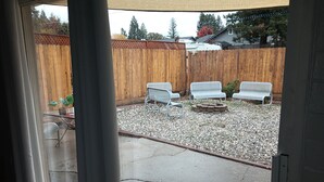 A backyard with a wooden fence, a fire pit, and two white metal chairs.