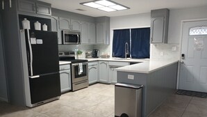 A modern kitchen with grey cabinets, stainless steel appliances, and a tiled floor.