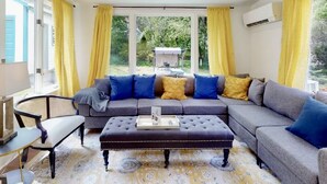 A living room with a grey sectional sofa, a black ottoman, and yellow curtains. - Lone Pine Cottage Maine - Chef’s Kitchen (Bath)