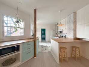 A modern kitchen with white cabinets, a wooden countertop, and a view of the city through large windows.