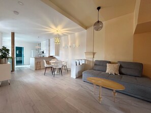 A modern living room with a grey sofa, a wooden coffee table, and a dining area with a white table and chairs.