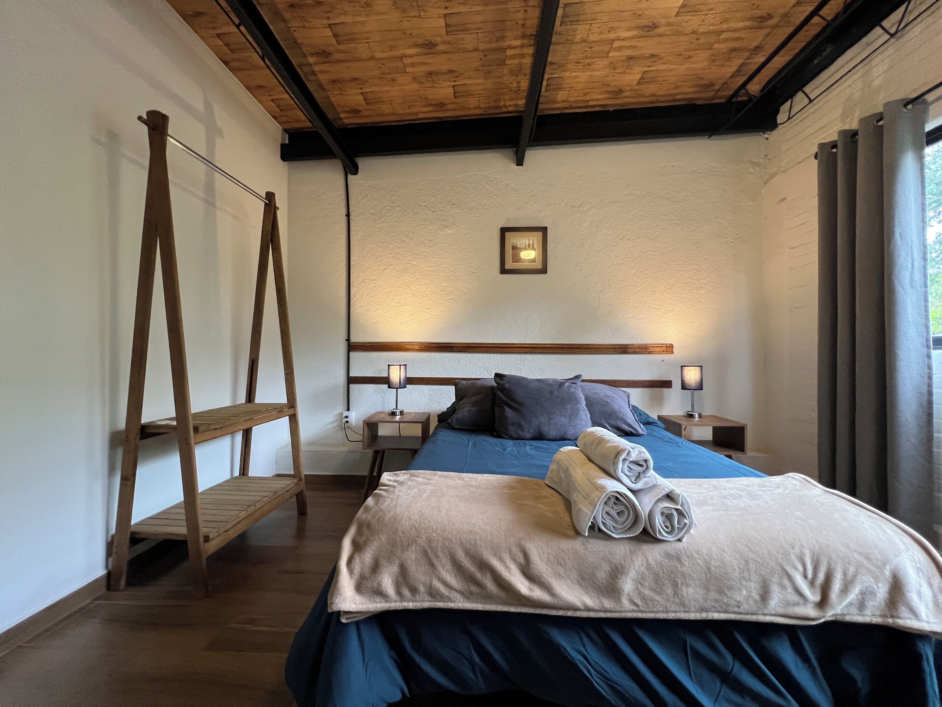 A bedroom with a wooden ladder, a bed with blue bedding, a wooden headboard, and a bedside table with a lamp.