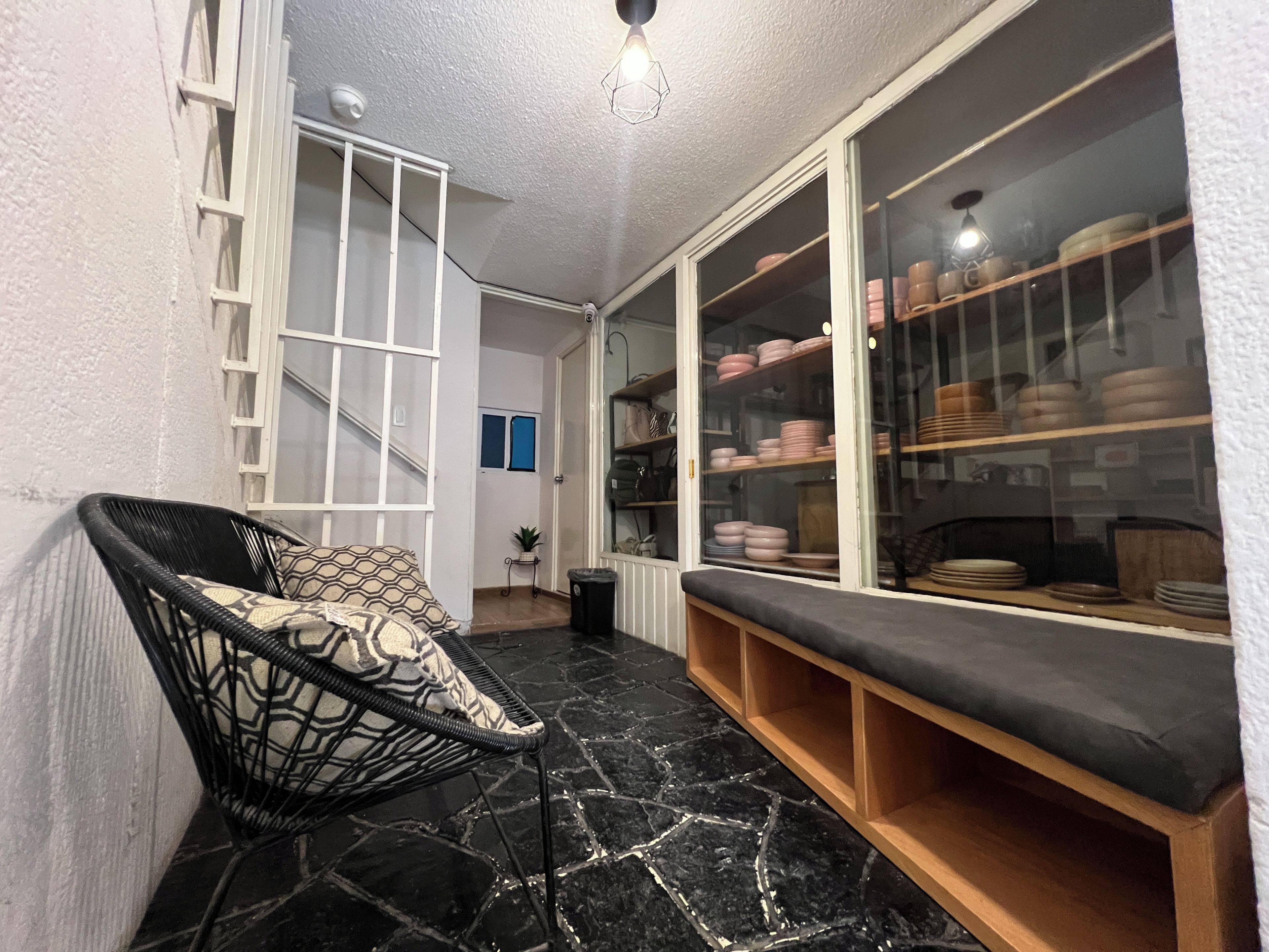 A room with a black marble floor, a wicker chair with a patterned cushion, a wooden bench, and a glass cabinet with dishes.