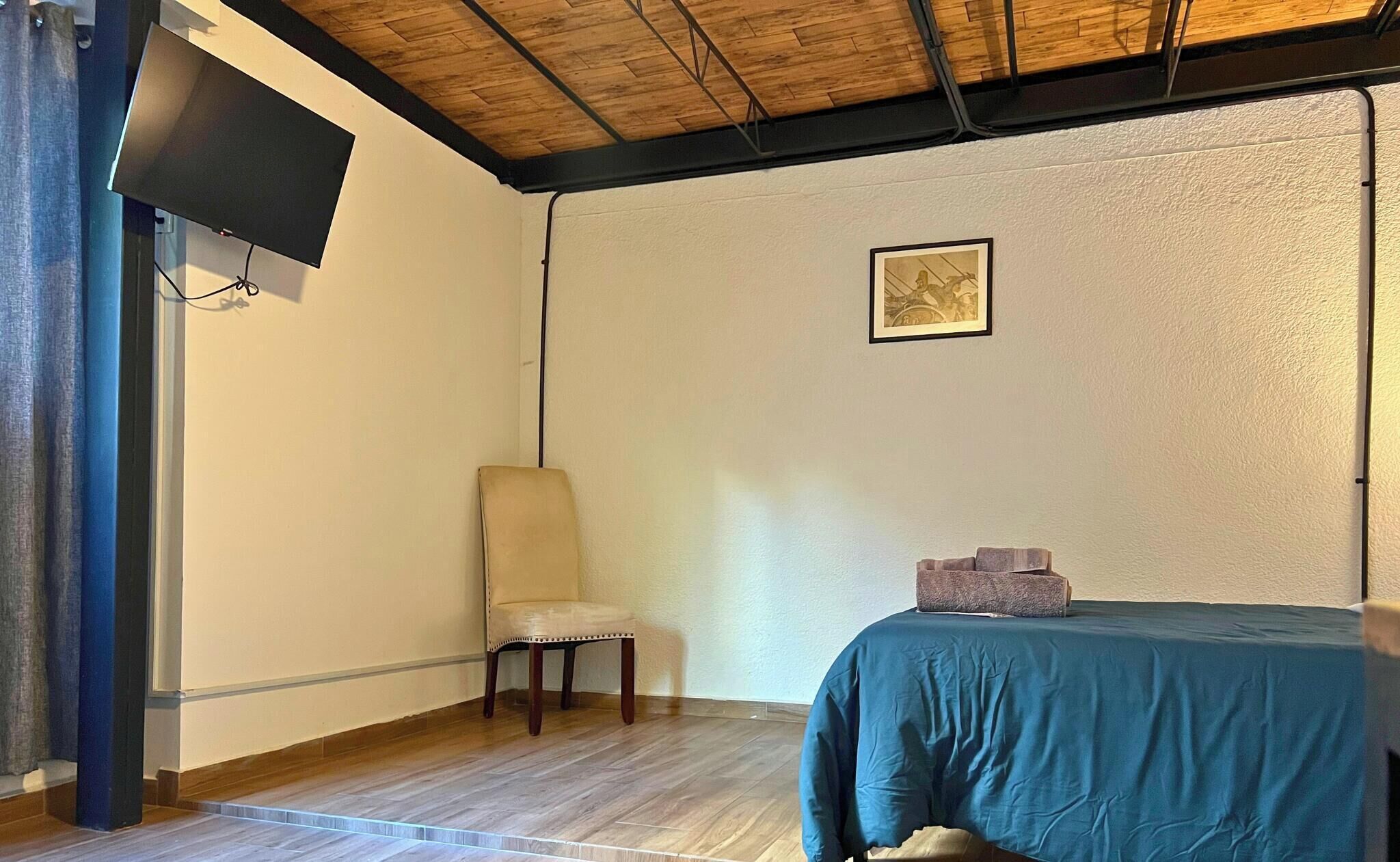 A room with a bed, a chair, a television mounted on the wall, and a framed picture.