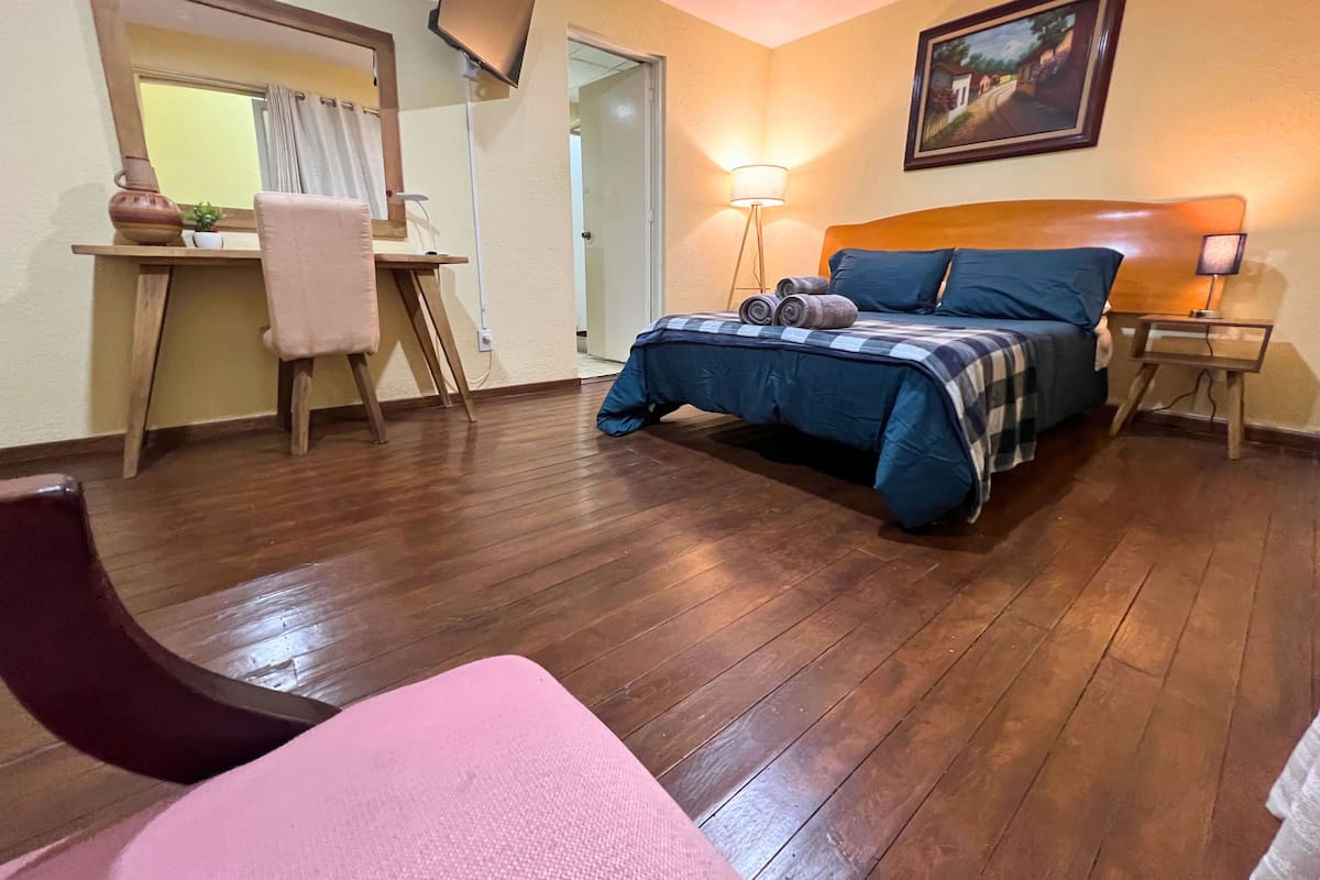 A bedroom with a bed, bedside tables, a desk, a chair, a TV, and a painting on the wall.