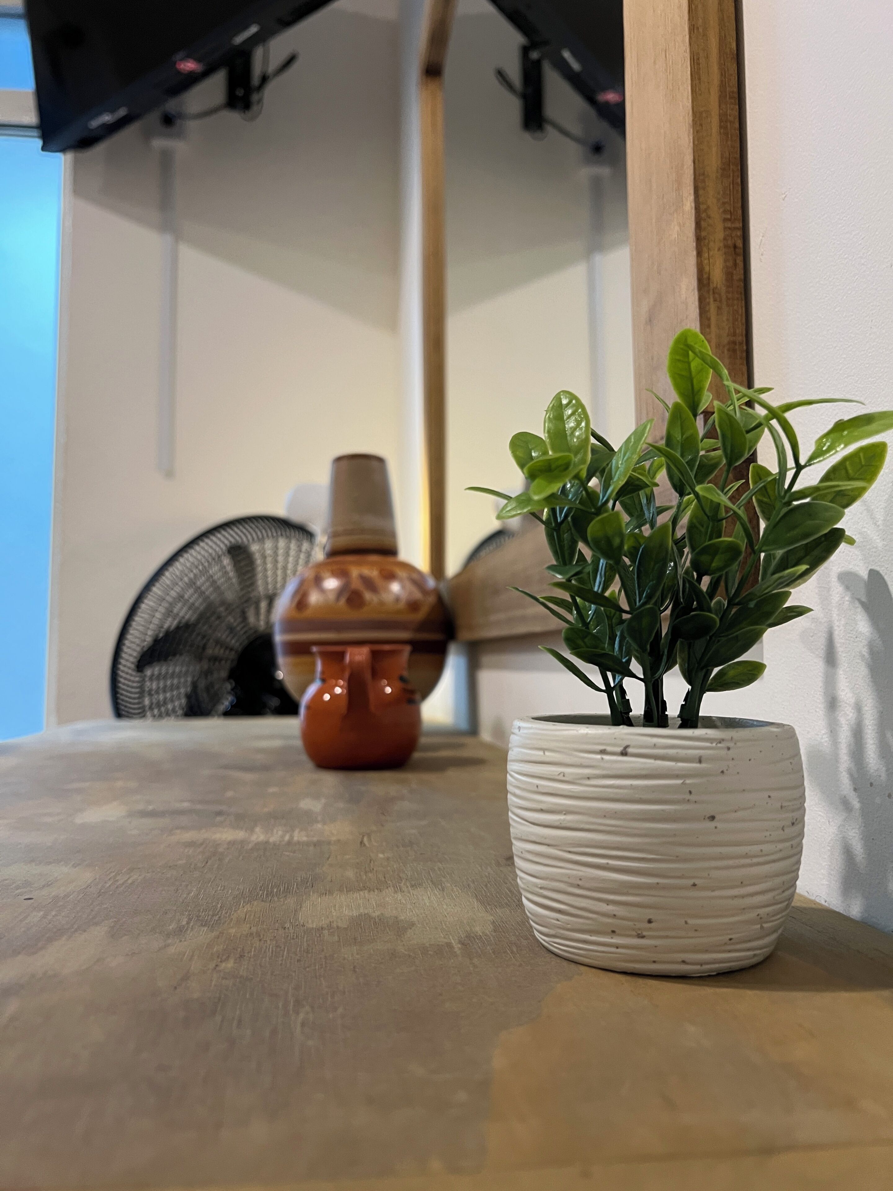 A potted plant on a table, a ceramic vase, and a fan in a room with a wooden beam ceiling.