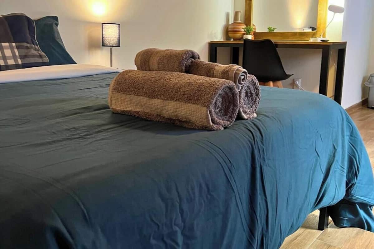 A neatly made bed with rolled towels, a desk with a mirror, and a chair in a modern room.