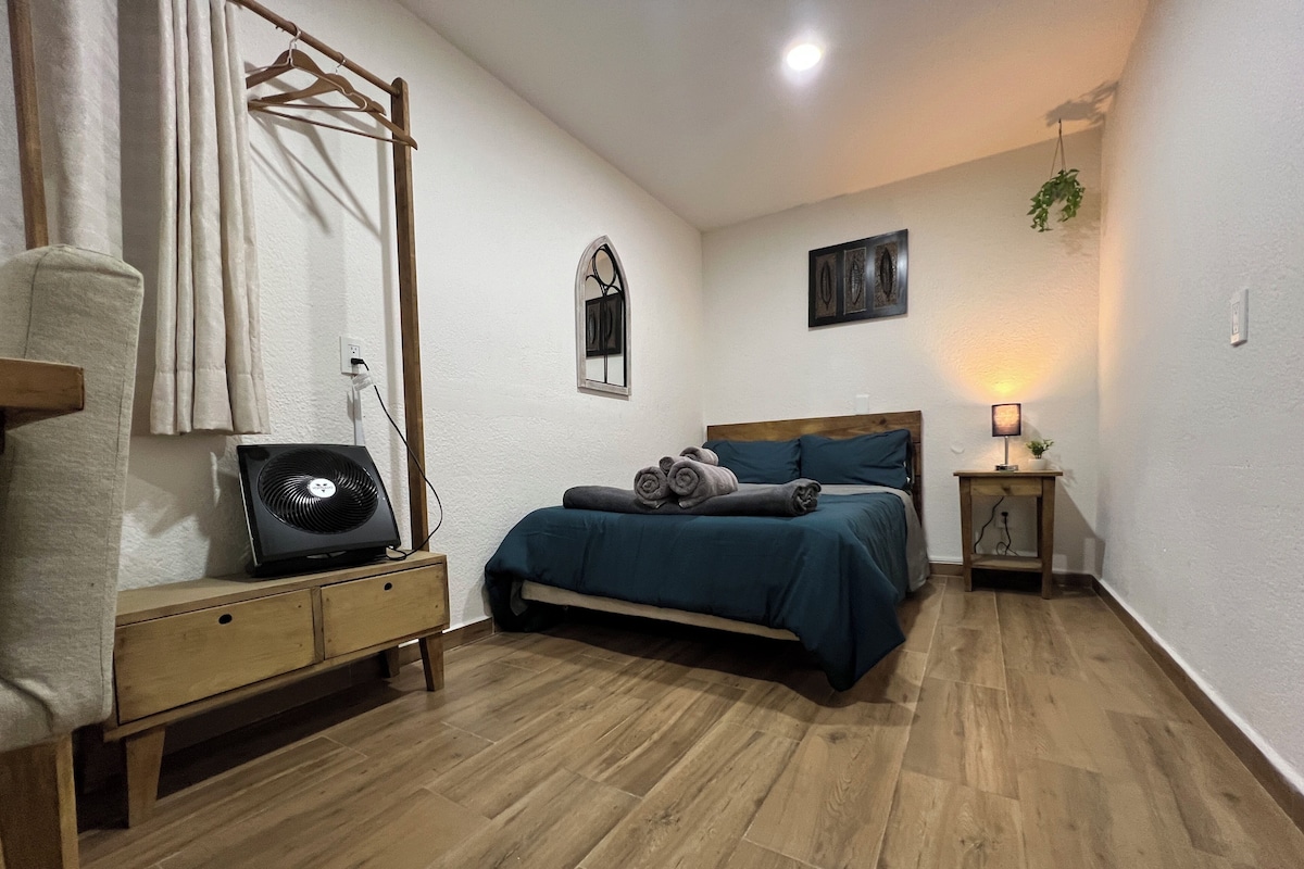 A bedroom with a bed, bedside table, lamp, and a fan.