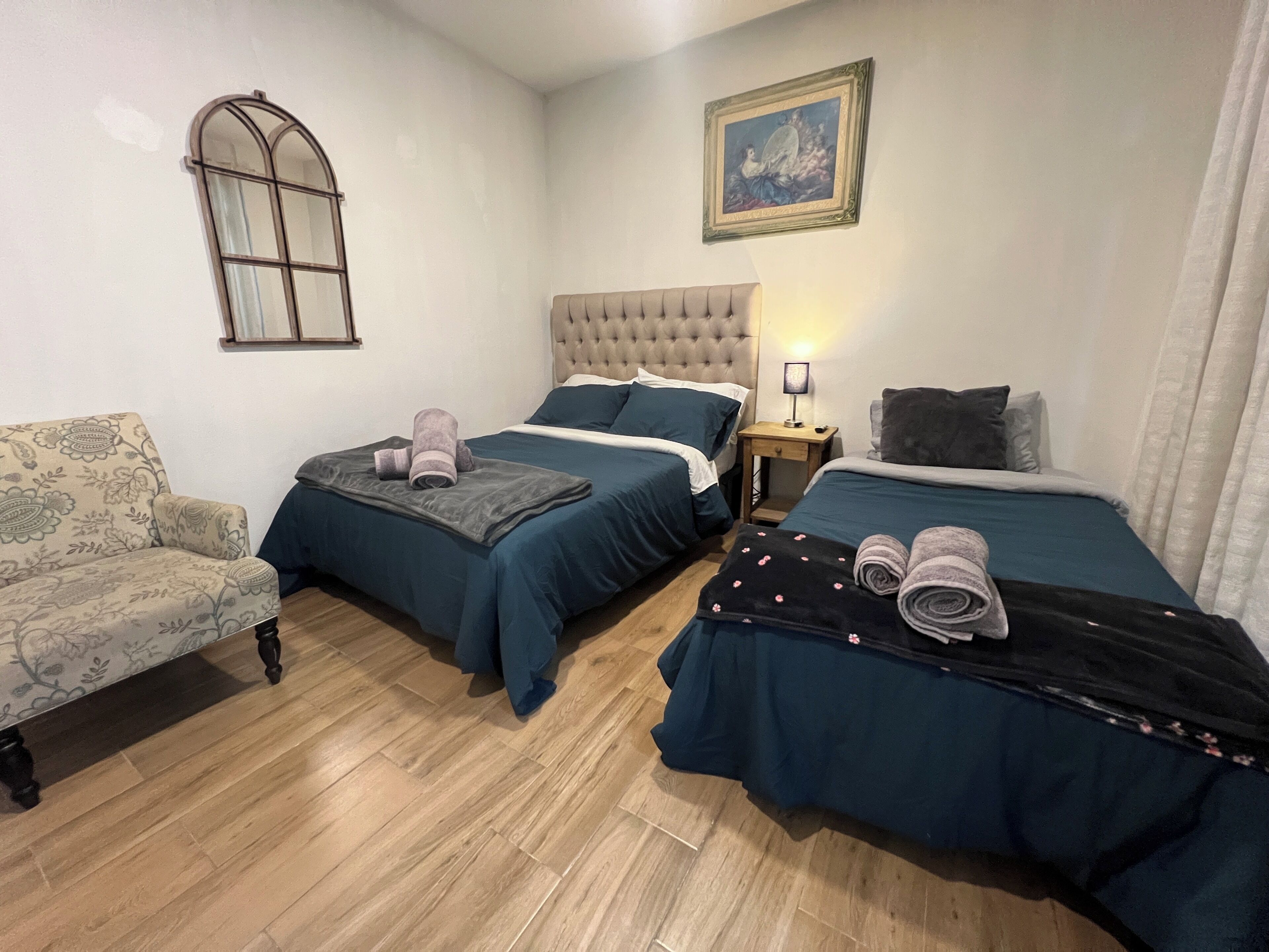 Een slaapkamer met twee bedden, een stoel, een nachtkastje, een lamp en een schilderij aan de muur.