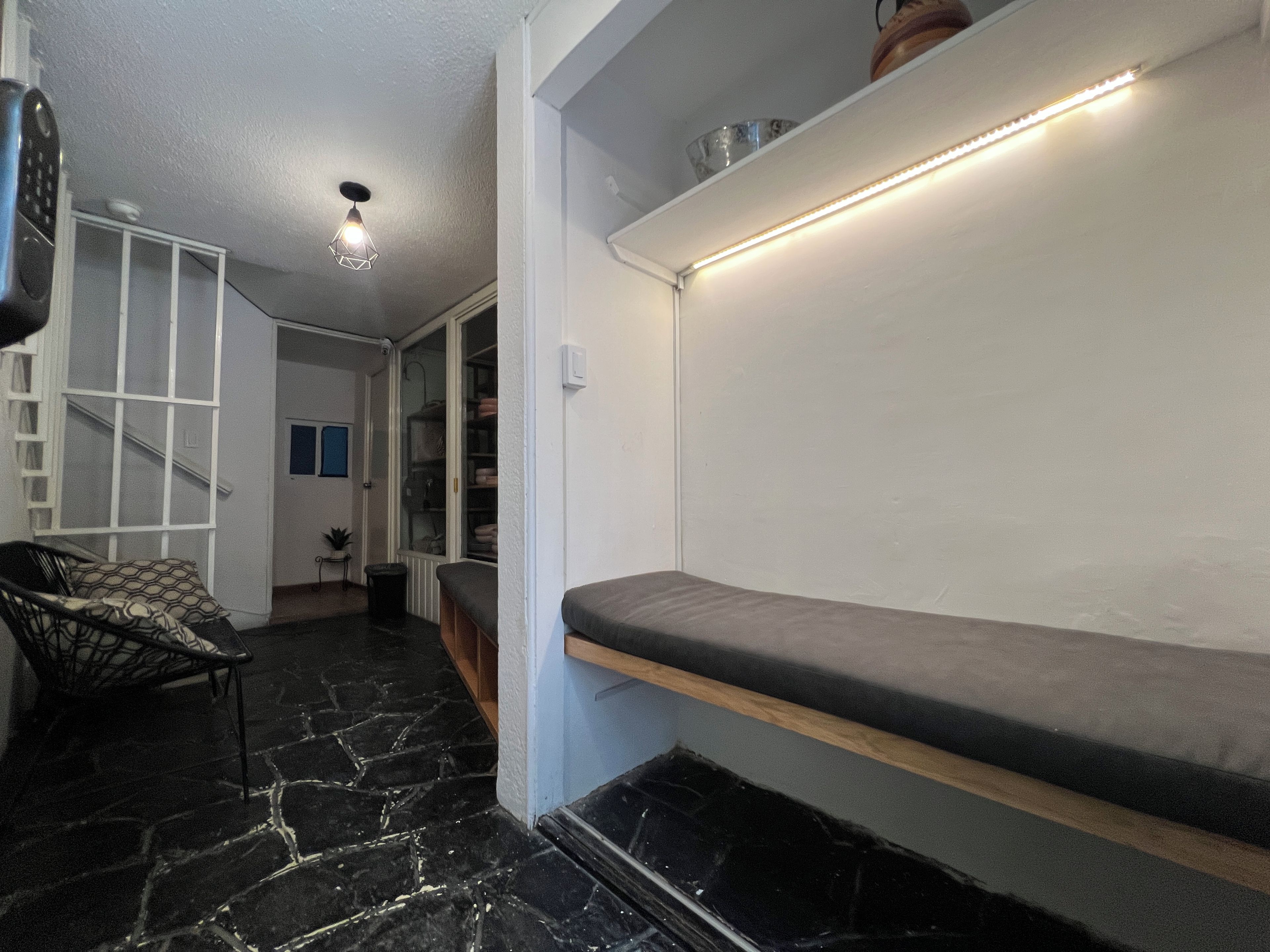 Un couloir avec un banc, un escalier et une porte donnant sur une pièce.