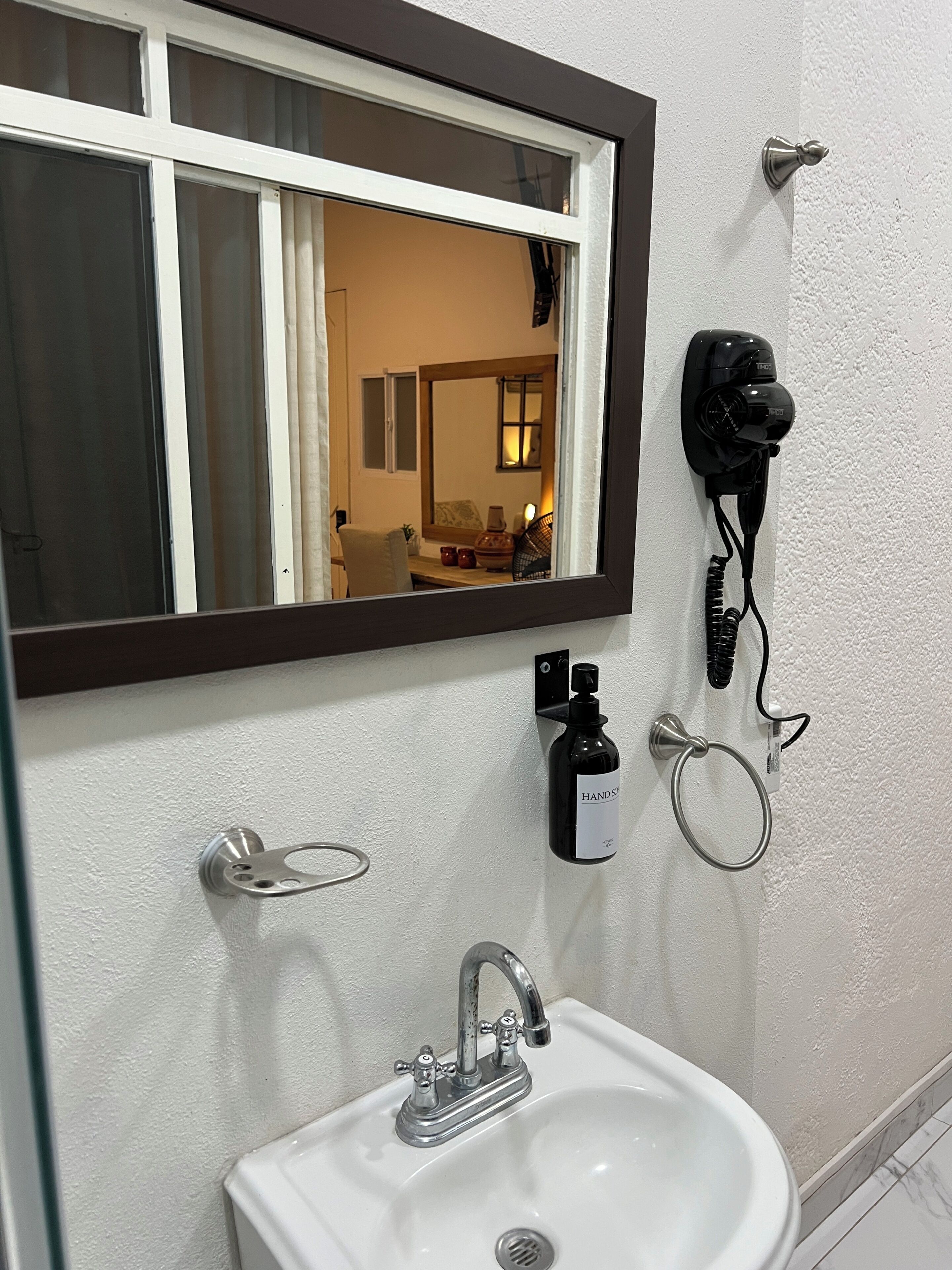 A bathroom with a white sink, a mirror, a window, and a hairdryer mounted on the wall.