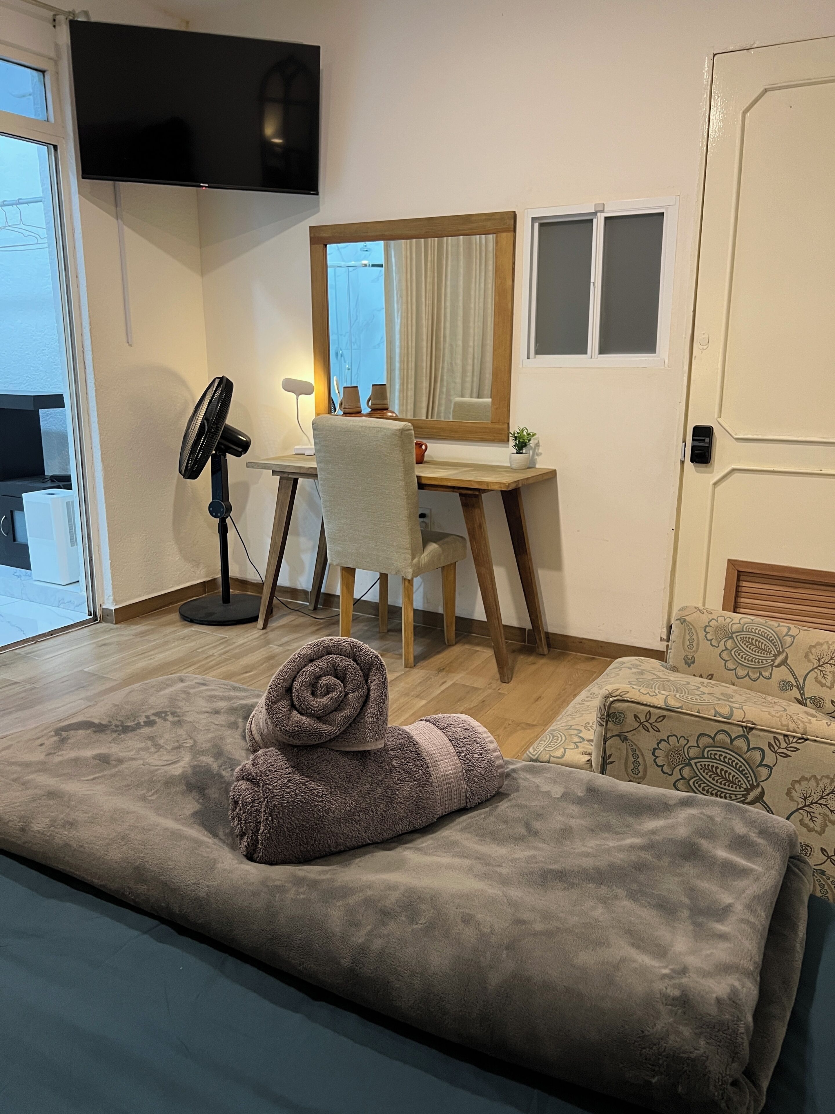 A room with a bed, a desk, a chair, a TV, and a door.