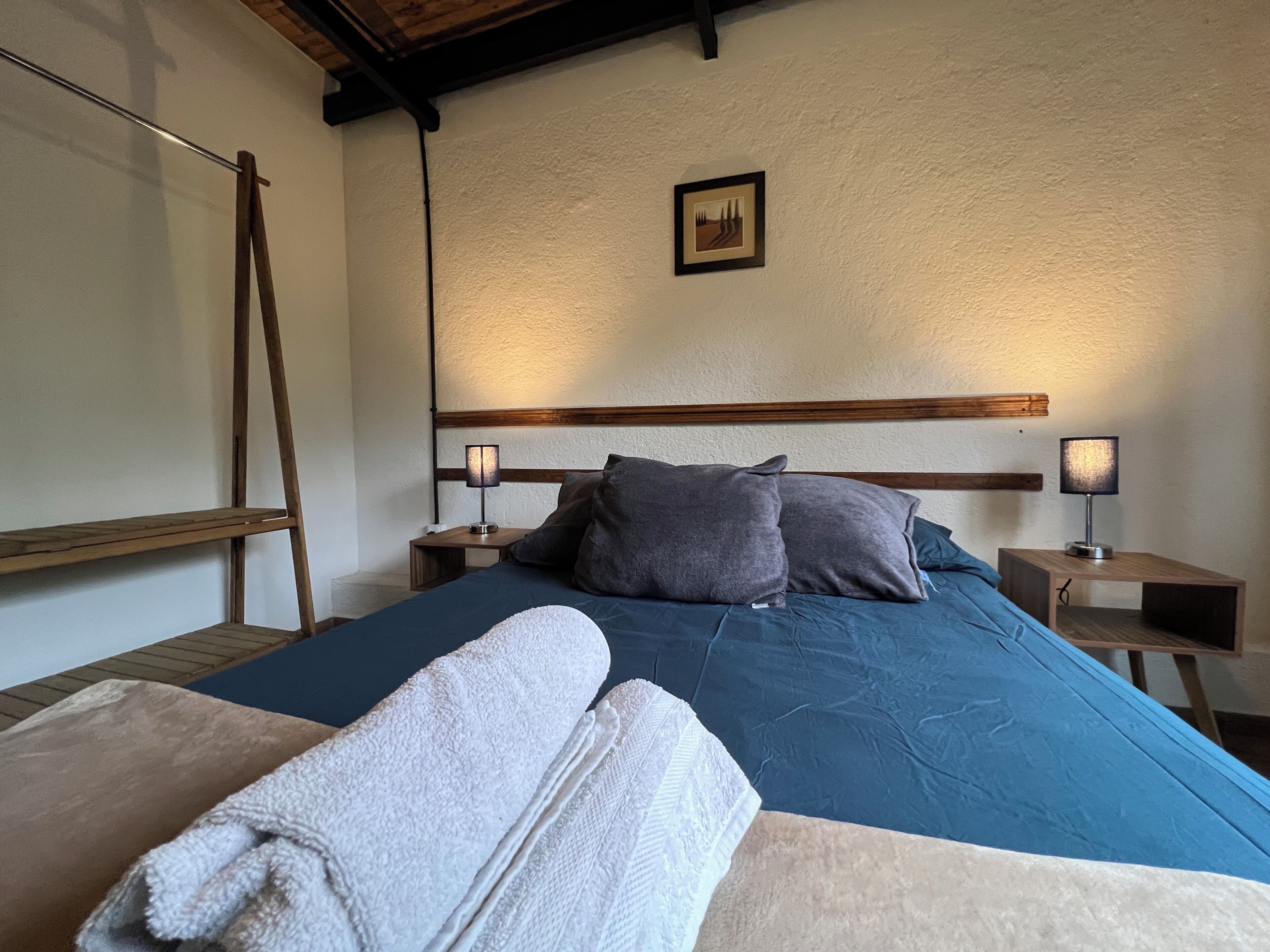 A bedroom with a bed, two bedside tables, a wall-mounted picture, and a wooden ladder.