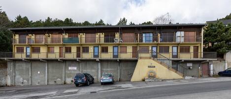 A multi-story building with balconies, a staircase, and a parking area with cars.