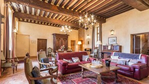 Ein geräumiges Wohnzimmer mit hoher Decke, Holzbalken und einer Chandelieber. Zwei rote Ledersofas, ein Couchtisch aus Holz und ein gemustertes Teppich sind vorhanden.