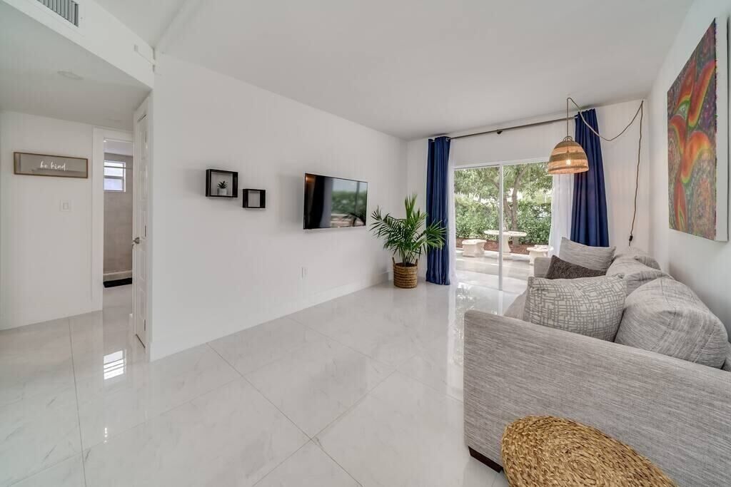 Un salon spacieux avec un grand canapé, un téléviseur à écran plat fixé au mur, une plante en pot et une vue sur l’extérieur grâce à de grandes fenêtres.