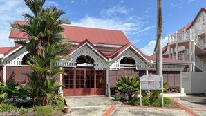 A building with a red roof and white architectural details, surrounded by tropical plants. - Tropicanavibes - Vue mer à Sainte-Luce (Sainte-Luce)