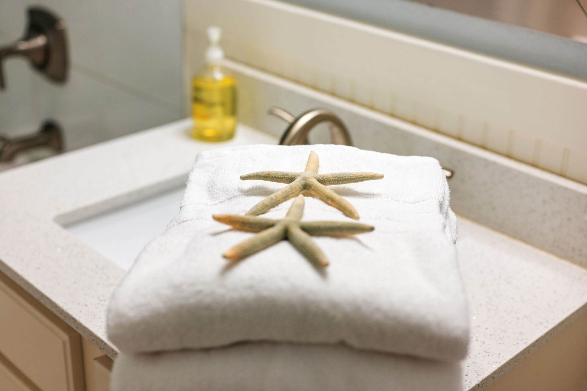 A bathroom with a white countertop, a towel with starfish, a bottle of soap, and a faucet.