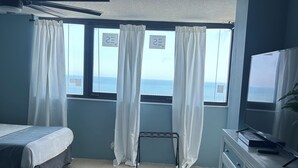 Ein Zimmer mit Bett, Schreibtisch, Deckenventilator, Fernseher und Meerblick.