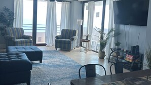 Ein großzügiges Wohnzimmer mit großem Fernseher, zwei Sofas, einem Esstisch und Meerblick.