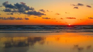 Ein Strand bei Sonnenuntergang, die Sonne versinkt im Meer.