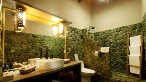 Ein Badezimmer mit Steinwand, Waschbecken mit Spiegel, Toilette und Handtuchhalter.