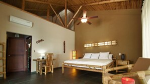 Ein Zimmer mit Bett, Stuhl, Tisch mit Kerze, Deckenventilator und Fenster mit Jalousien.