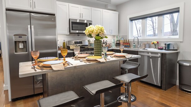 A modern kitchen with stainless steel appliances, a central island with bar stools, and a window providing natural light.