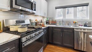 A modern kitchen with stainless steel appliances, white cabinets, and a wooden floor.