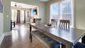 A dining area with a long table, benches, and a hanging light fixture. - 2BR Family Charmer Duplex near Drake (Des Moines)