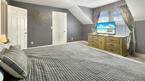 A bedroom with a bed, a TV on a dresser, a ceiling fan, and a window with curtains. - 2BR Family Charmer Duplex near Drake (Des Moines)