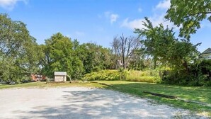 A spacious outdoor area with a gravel path, surrounded by lush greenery and trees. - 2BR Family Charmer Duplex near Drake (Des Moines)