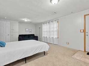 Une chambre à coucher avec un lit, un canapé de couleur sombre, des rideaux blancs et une porte.