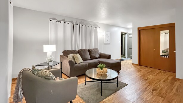 A modern living room with a sofa, armchair, and coffee table, a wooden floor, and a door with a mirror. - Family Friendly 3 BR 2 Bath Duplex Sleeps 9! (Des Moines)