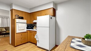 A compact kitchen with wooden cabinets, a white refrigerator, and a microwave. There's a dining table with a plant and a patterned placemat. - Family Friendly 3 BR 2 Bath Duplex Sleeps 9! (Des Moines)