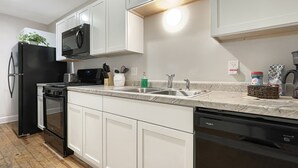 Une cuisine moderne avec des meubles blancs, un réfrigérateur noir, un four à micro-ondes, une cuisinière, un évier et un lave-vaisselle.