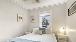 Une chambre à coucher avec un lit, une table de chevet, une fenêtre et un tableau encadré au mur.
