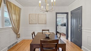 A dining room with a wooden table, chairs, a chandelier, and artwork on the wall.