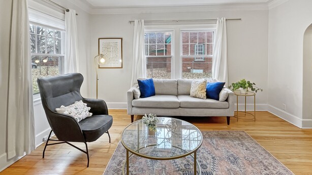 A living room with a grey sofa, a black chair, a glass coffee table, and a patterned rug.