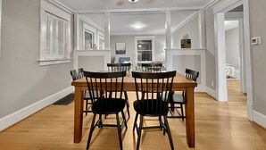 A dining area with a wooden table and chairs, white walls, and a ceiling fan.