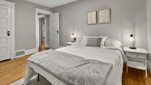 A bedroom with a large bed, bedside tables with lamps, a door, and a vent.