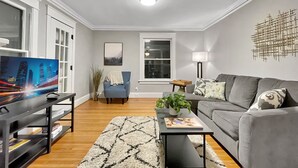 A modern living room with a flat-screen TV, a grey sofa, a coffee table, and a patterned rug.