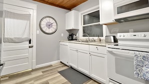 A kitchen with white cabinets, a clock, a stove, and a coffee maker.