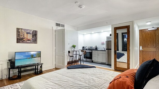 Una habitación compacta con cama, televisión, kitchenette y una puerta que da a otra habitación.