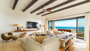 Ein geräumiges Wohnzimmer mit einer großen Couch, einem Couchtisch und einem Fernseher. Ein Balkon bietet Blick aufs Meer.
