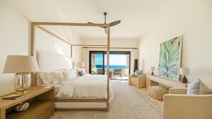 Ein geräumiges Schlafzimmer mit Himmelbett, einer Sitzecke inklusive Sofa und Sesseln, einem großen Gemälde und Meerblick durch eine offene Tür.